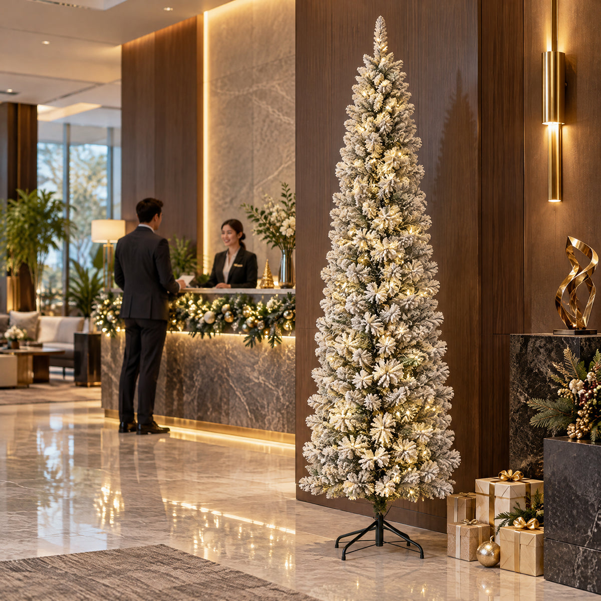 Tall slim flocked artificial Christmas tree with warm LED lights and a metal stand decorating a modern corporate lobby beside reception desks and holiday gifts.