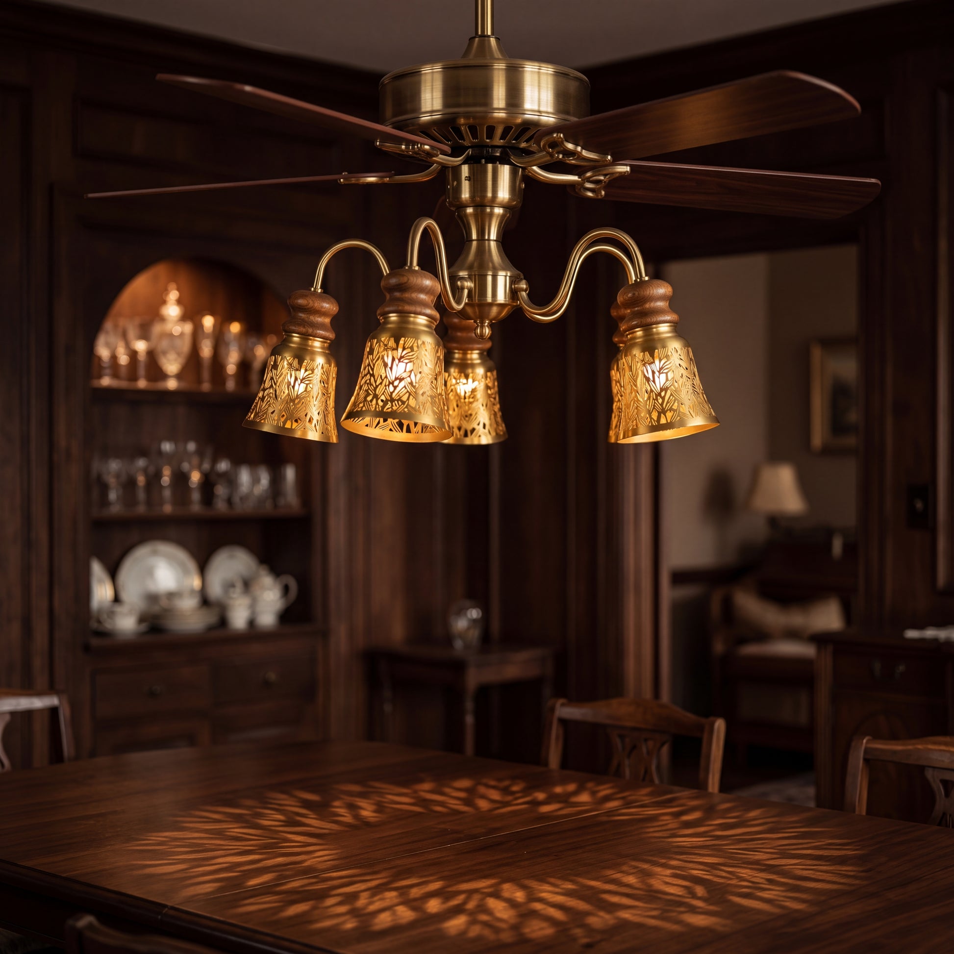 Laser-cut starburst metal lamp shade set of 4 pack clip-on small decorative shades installed on vintage brass ceiling fan light kit, antique bronze exterior with gold interior laser cut starburst leaf flower pattern creating retro lighting effects and warm light shadow projection on dark wood dining table, ideal lamp shade replacement for ceiling fan lights pendant lights chandeliers and vintage modern interior home decor upgrades