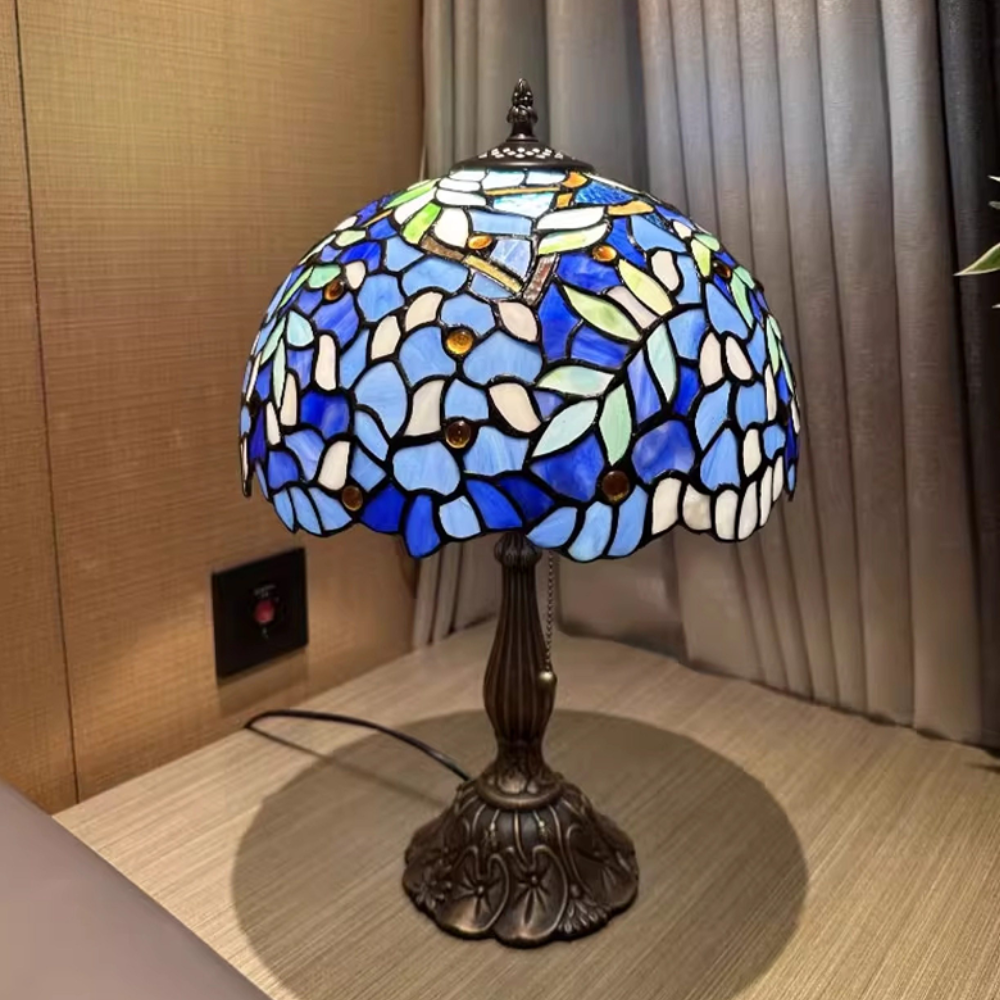 Tiffany style table lamp casting a soft ethereal glow through blue wisteria stained glass in calming interior space