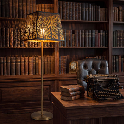 Modern square metal clip-on lamp shade on brass floor lamp, black and gold woodland tree pattern, industrial minimalist replacement lamp shade casting warm ambient glow in vintage library
