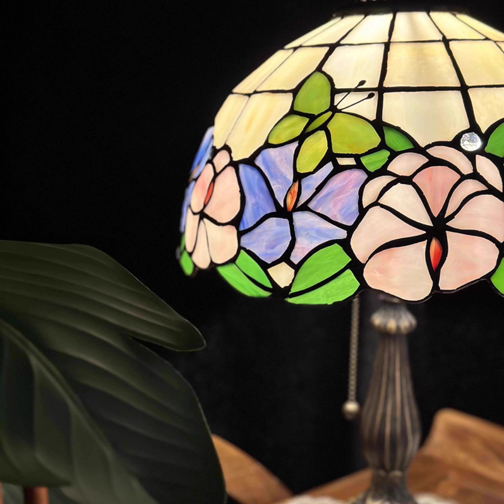 Tiffany style table lamp casting a warm romantic glow through pastel floral stained glass in bedroom setting