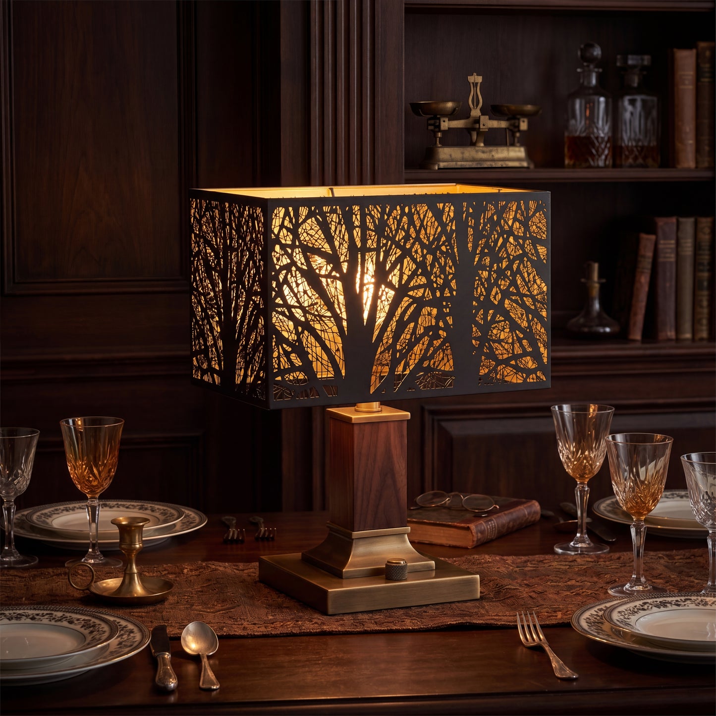 Rectangular Metal Lamp Shade with Laser-Cut Tree Pattern on Modern Walnut Wood and Brass Square Base Table Lamp Placed on Elegant Formal Dining Table Set for Dinner - Antique Brass Balance Scale on Dark Wood Shelf in Background, Vintage Apothecary Glass Bottles, Leather Books, Crystal Amber Wine Glasses and Clear Water Goblets, Fine China Plates with Decorative Gilt Rim, Gold Flatware Silverware, Pair of Round Wire-Rim Eyeglasses on Antique Leather Book, Brown Textured Table Runner - Matte Black Metal Exter