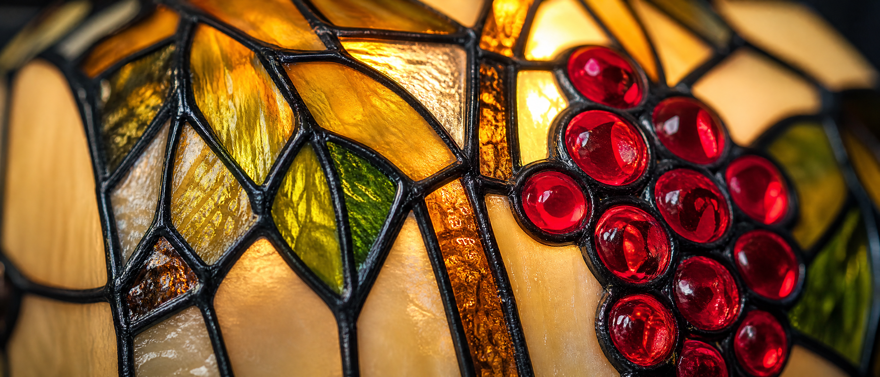 Close-up of Tiffany style banker lamp stained glass shade with red grapes, green leaves and warm amber glass