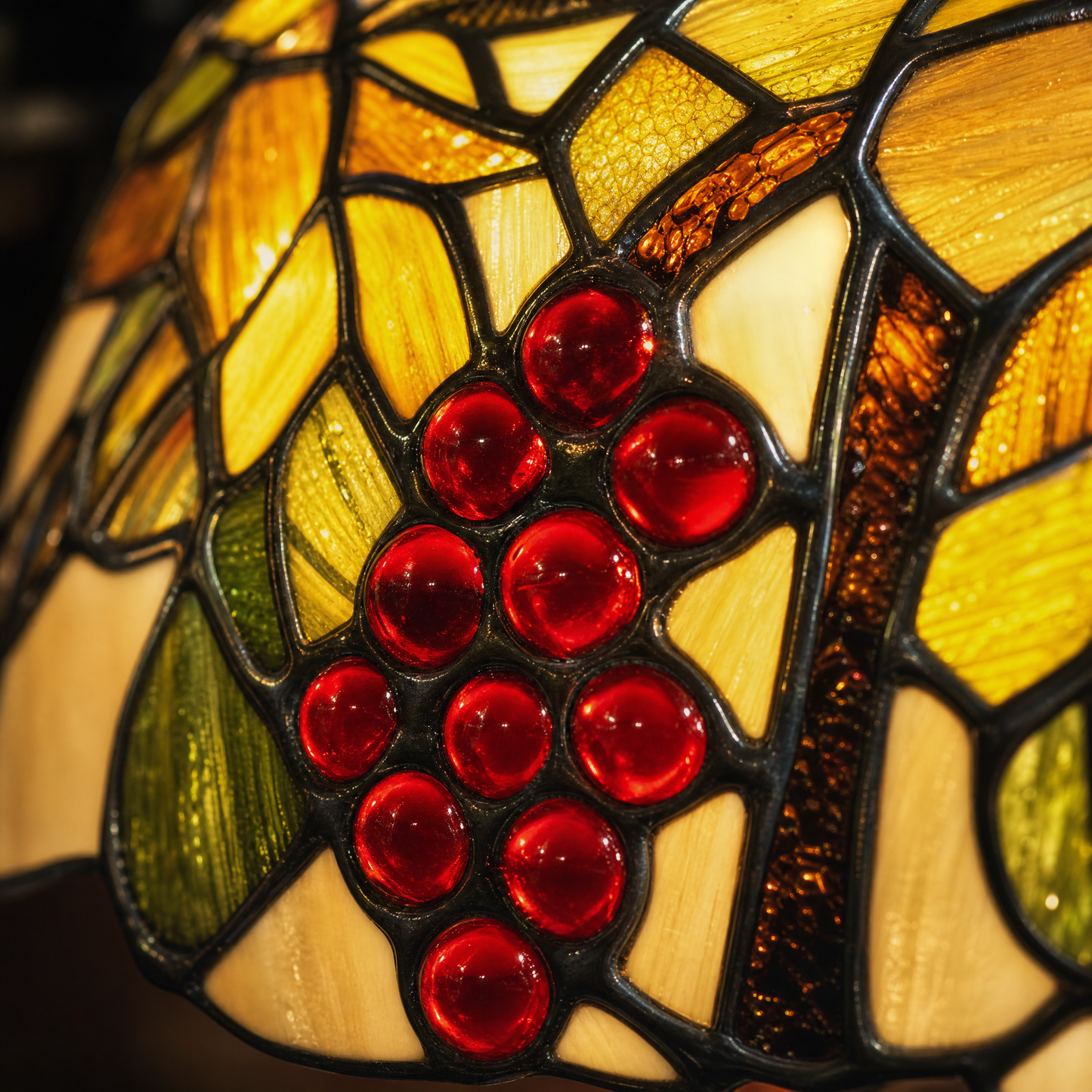 Close-up of Tiffany style banker lamp stained glass shade with red grape, green leaf and amber glass details